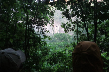 John Zeiger (left) and Justin Proctor (right) stand firm against the rain and mosquitos during an evening observation session of Ram Goat Cave (black spot in center of photo). (Photo by Seth Inman)