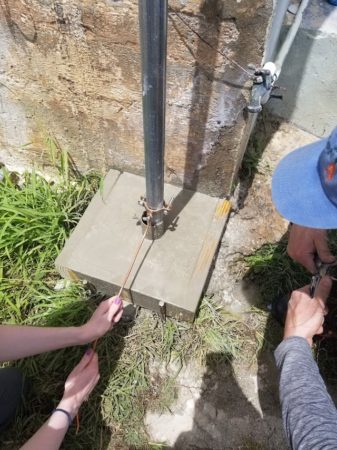Mallory Sarver and Aarron Collman install the grounding rod, connecting it to the mast over the concrete base that has been poured earlier that day.