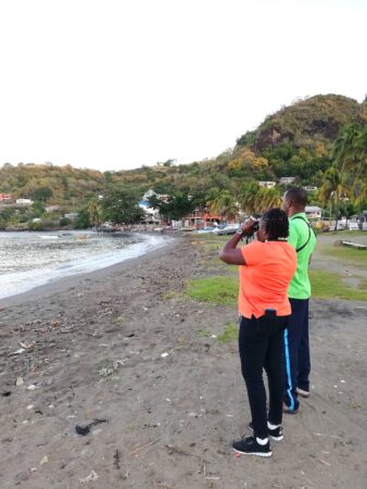 Photo of a man and woman birdwatching on the shore.
