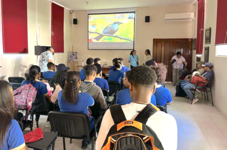 Photo of students sitting in a classroom facing forward. The title slide of the presentation is project onto the wall and has a photo of a bird.
