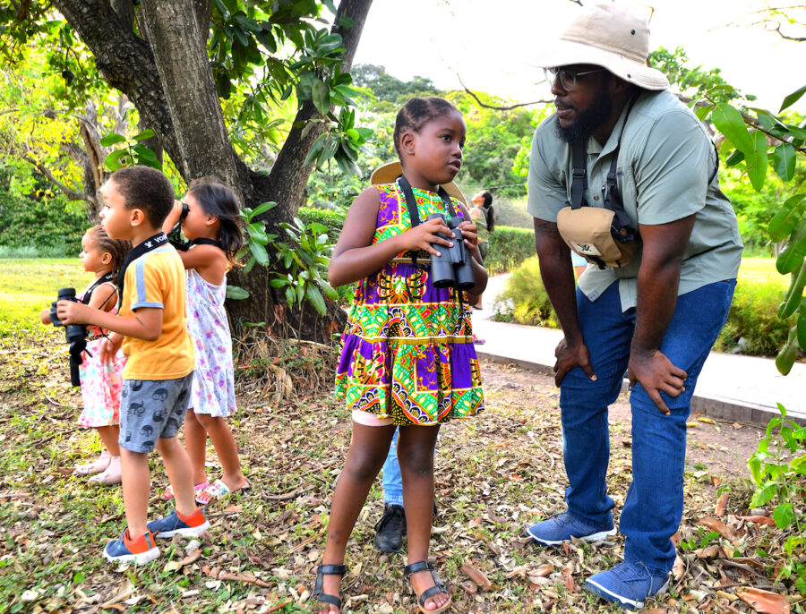 Photo of group of children birdwatching. In the photo a girl, with binoculars draped around her neck speaks with a man.