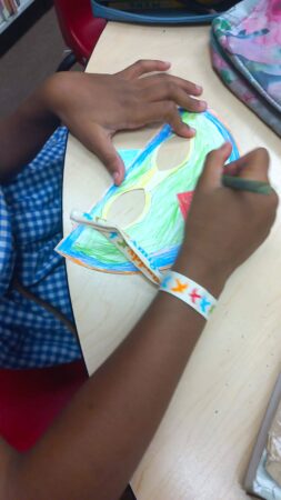 A child coloring a bird mask with crayons.