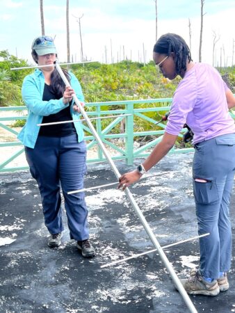 Photo of two women assembling an antenna- one is behind holding it above the floor at an angle and the other is in front attaching the individual antenna to the boom. 