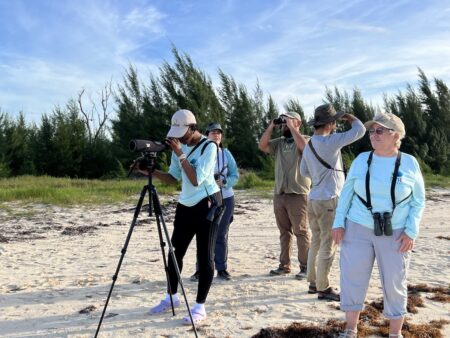 Photo of group of people birdwatching on a beach.