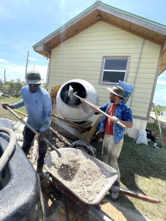 Photo of two men shoveling cement into a mixer