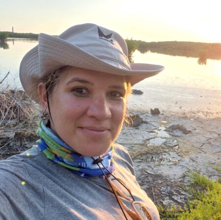 Selfie of a woman wearing a hat and buff around her neck in a swamp