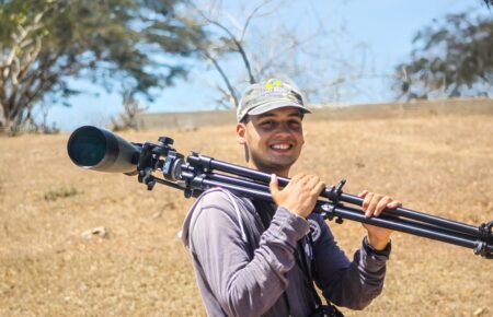 photo of man holding spotting scope over his should and smiling at the camera