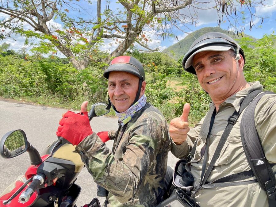 Selfie of two men on an electric scooter, both are giving the thumbs up. 