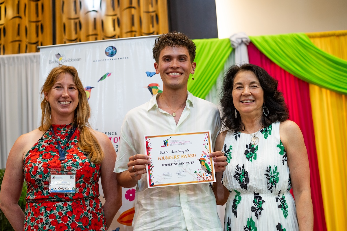 Photo of two women and one man facing the photographer while standing on stage. The man in the middle is holding a certificate.