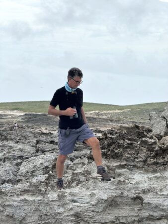 person walking along rocky shoreline with binoculars.