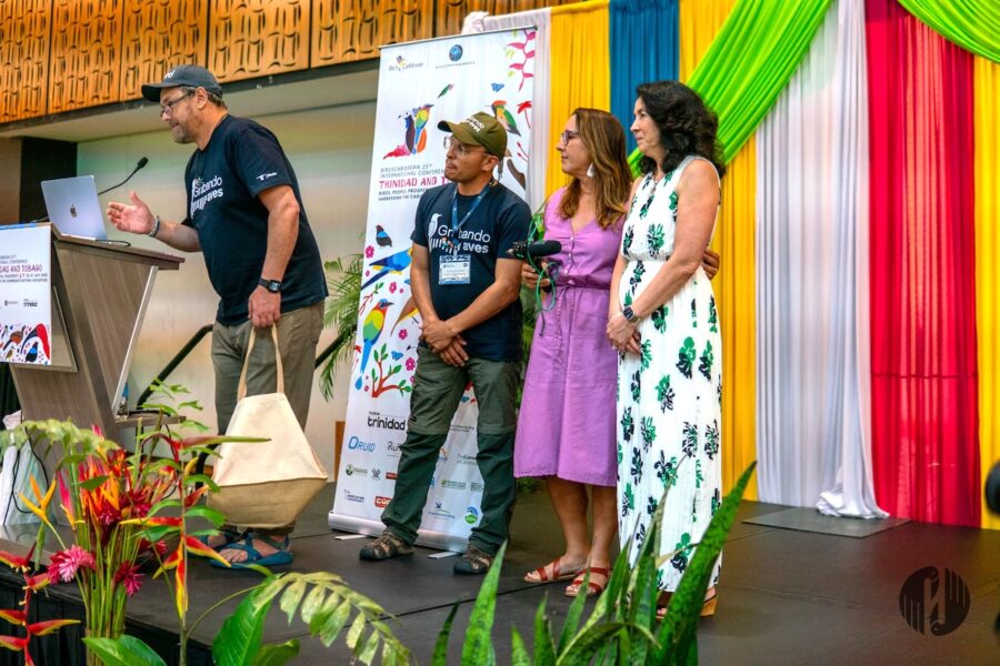 Photo of group of people on a stage. One man is at the podium while the other three (one man and two women) are standing behind him. 